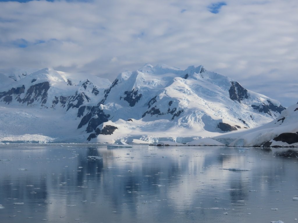 Massive snow covered glacial ice reflected in the waters of Antarctica.