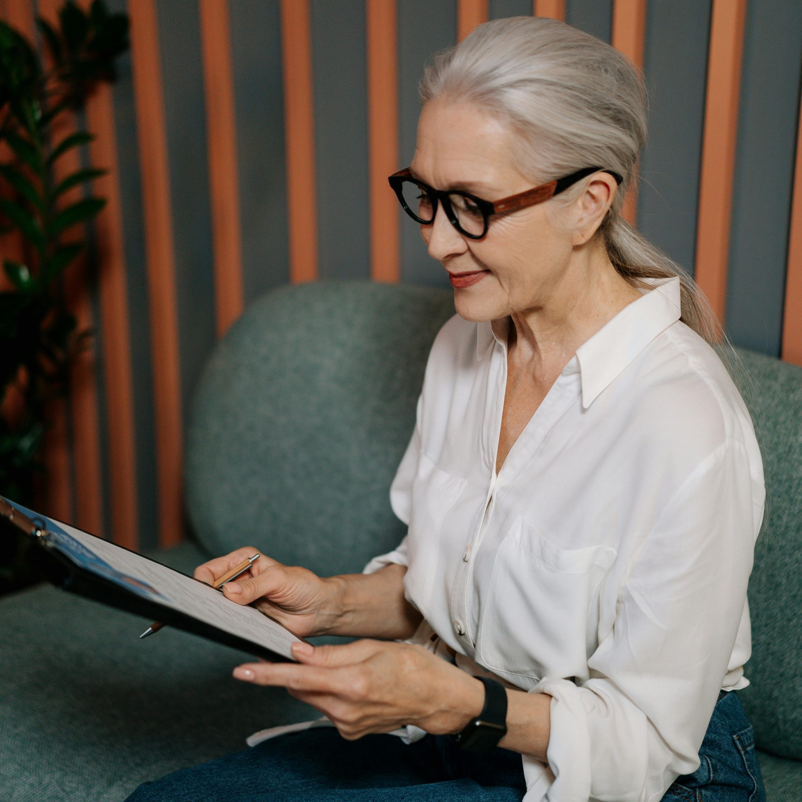 Woman sitting on couch looks over paperwork in her hand. Perhaps she is working on a plan to make a Bucket List?