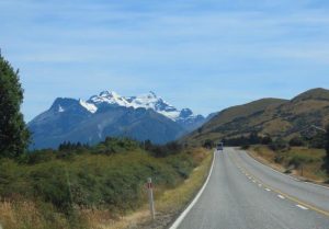 A road stretches towards towering mountains covered in snow on the South Island of New Zealand.