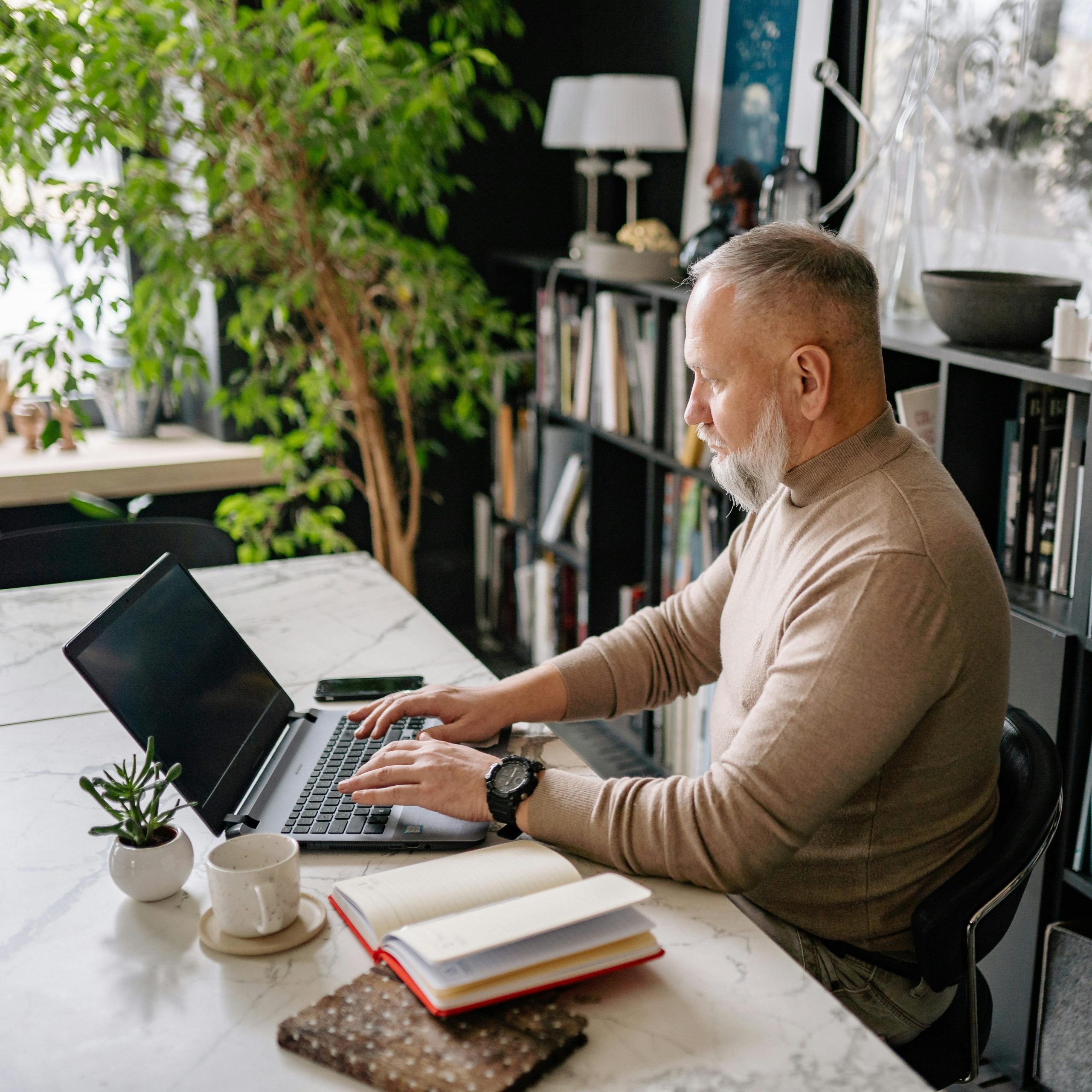 Thinking about things you want to accomplish before your next milestone birthday is a great way to make a Bucket List. Man with beard working on laptop.