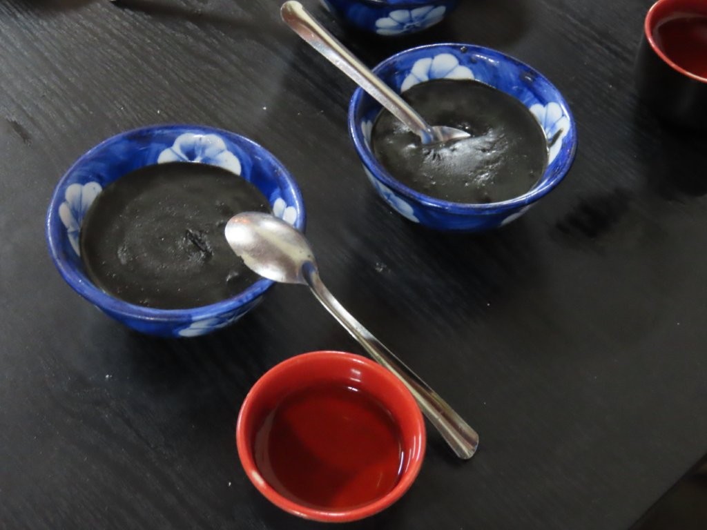 Two blue and white small bowls with spoons, and one red bowl contain black sesame soup.