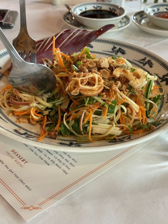 A bowl and spoon featuring thinly sliced carrot, papaya and other vegetables in a salad
