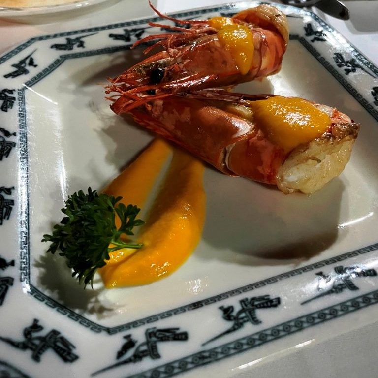 Two fried King Prawn pieces on a square plate with roasted melon pieces and parsley.