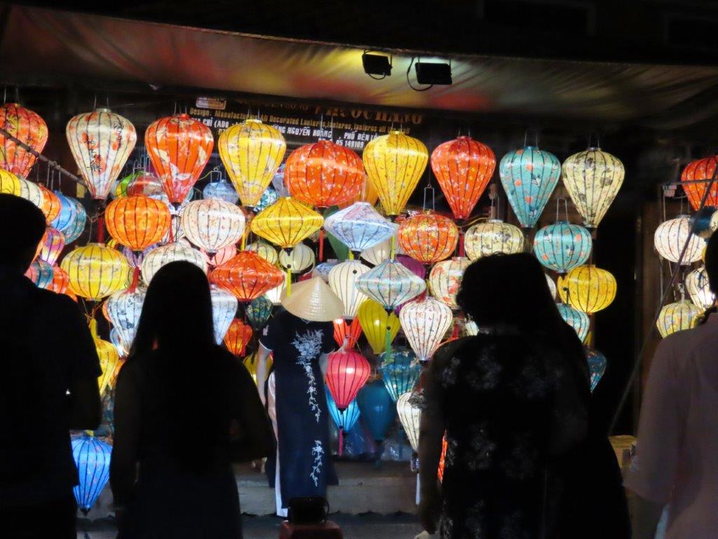 Crowds gather to observe a large group of colorful lanterns glowing in the night.