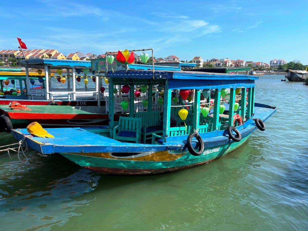 A colorful wooden boat in several shades of blue waits to take passengers on out the Thu Bon River. This boat holds 10-12 people where most of the boats are smaller. 