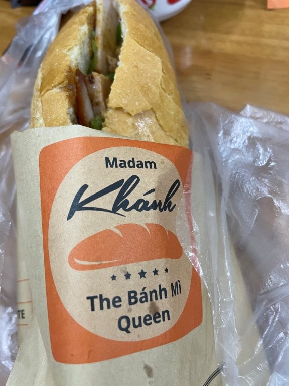Breaded sandwich wrapped in a paper bag that says Madam Khanh - the Bahn Mi Queen