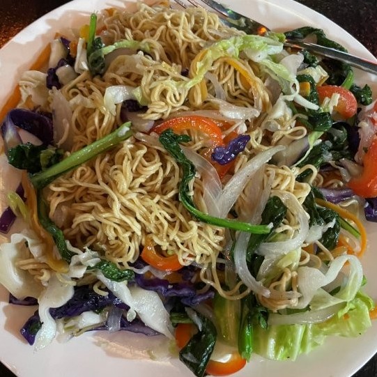 Fried noodles with lots of colorful vegetables on a white plate.