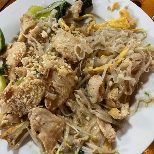 Thin rice Noodles, stir-fried chicken and vegetables served on a white plate.