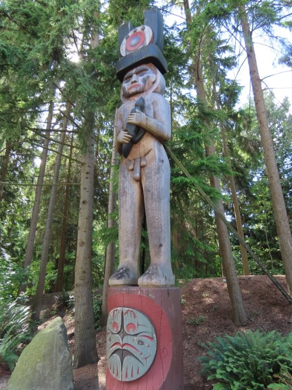 A tall wooden carving of a native man holding what appears to be a giant cucumber in his hands?