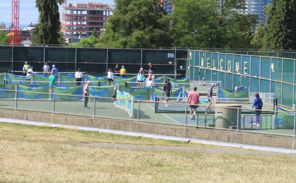 Players in colorful shirts play pickleball on crowded tennis courts at Queen Elizabeth Park in Vancouver. They are really jammed in there!