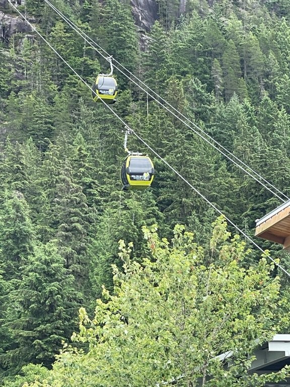 Two green gondolas move slowly along cables high in the sky as they take passengers from the Sea up to the Sky.