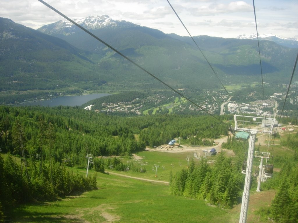 A view of the Blackbomb Ski Resort in summer shows empty chairlifts and lots of green grass. 