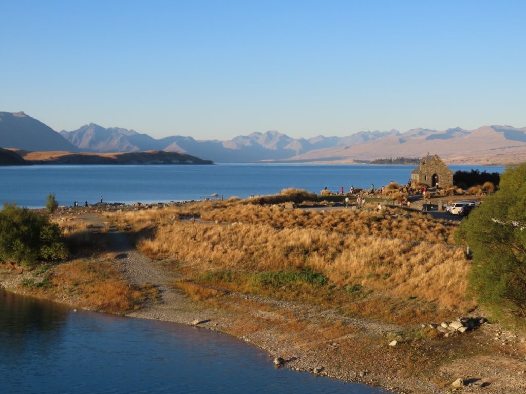 Brown grass on the hill with a beautiful turquoise lake and mountains in the background.