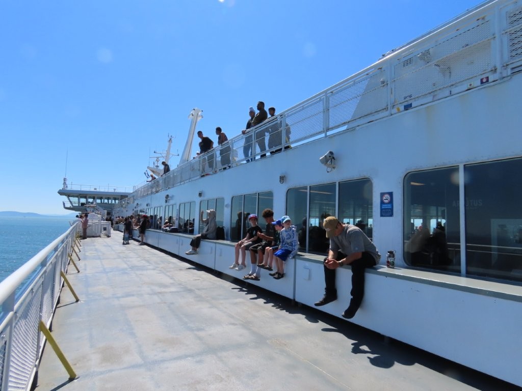 Passengers enjoying sunshine and sea views from the upper outdoor deck of a BC Ferries vessel.