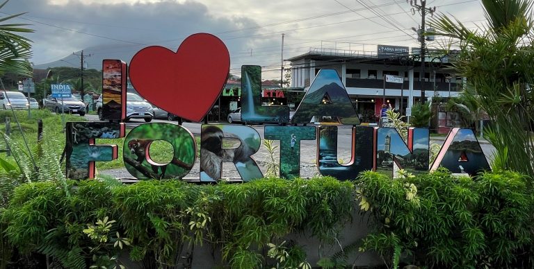 A colorful sign says I heart La Fortuna, surround by lush greenery.