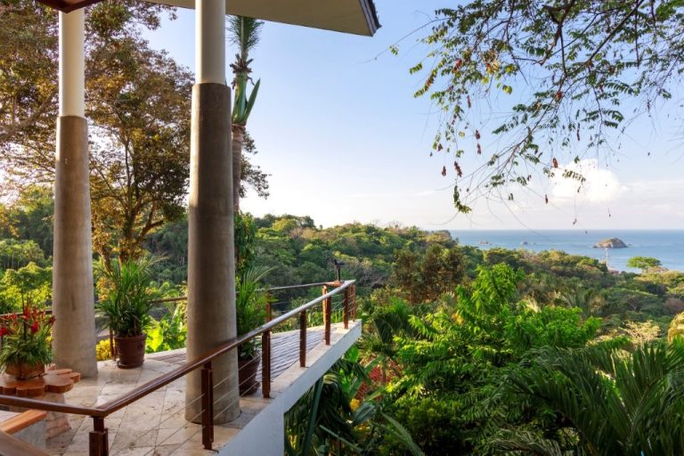 Ocean view from a scenic walkway at Si Como No, framed by trees and lush greenery