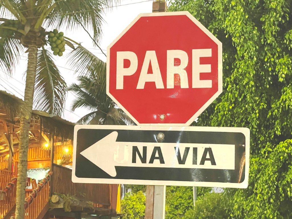 A red octagon with the word PARE in it is a Spanish Stop Sign. Underneath is a arrow pointing right with the words UNA VIA which means One Way in Spanish.