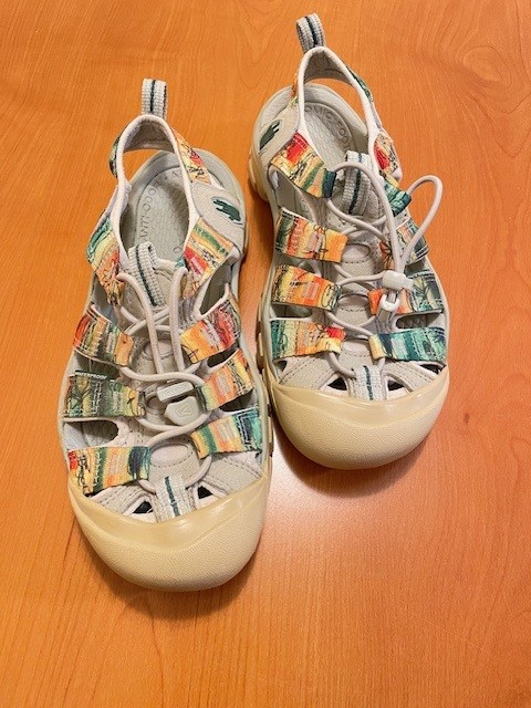 A colorful pair of sandals sits on a wooden table. 