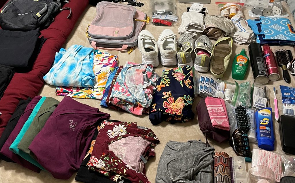 A variety of colorful clothes and toiletries are spread out on a bed with a brown blanket. This is Step 1 of figuring out what to pack for an African safari