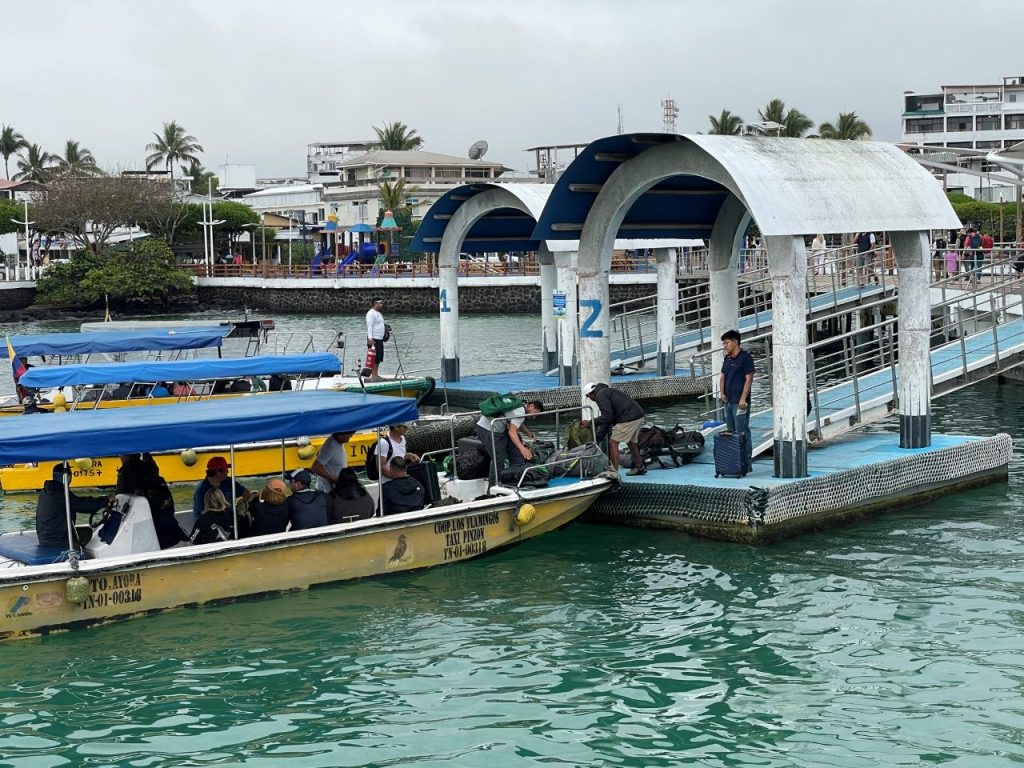 A yellow water taxi idles beside the pier as passengers climb out and luggage is passed up onto the dock. Water taxis are part of almost every Galapagos ferry transfer, so having small cash and keeping an eye on your bags makes the process much smoother.