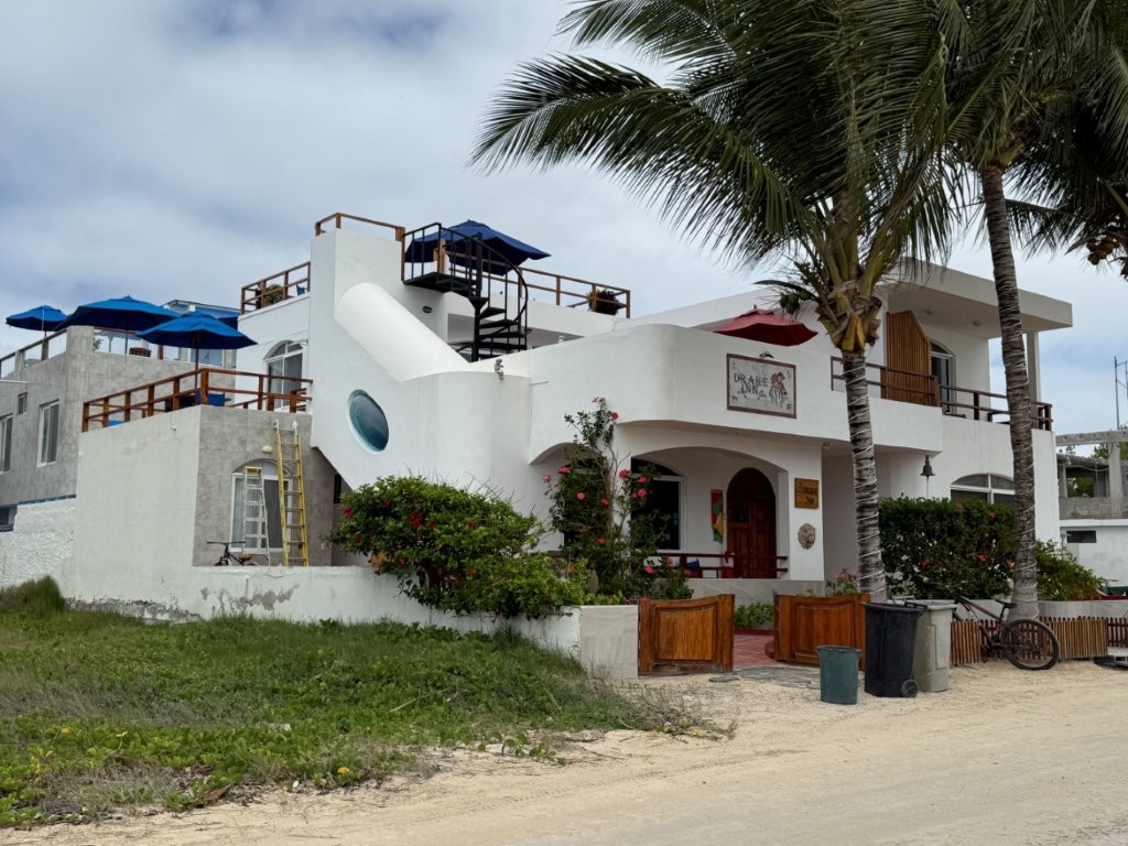 The white Drake Inn sits along a sandy road with palm trees, rooftop terraces, and a quiet beachside feel. Drake Inn is a strong budget-friendly option for travelers who want easy beach access on Isabela Island.