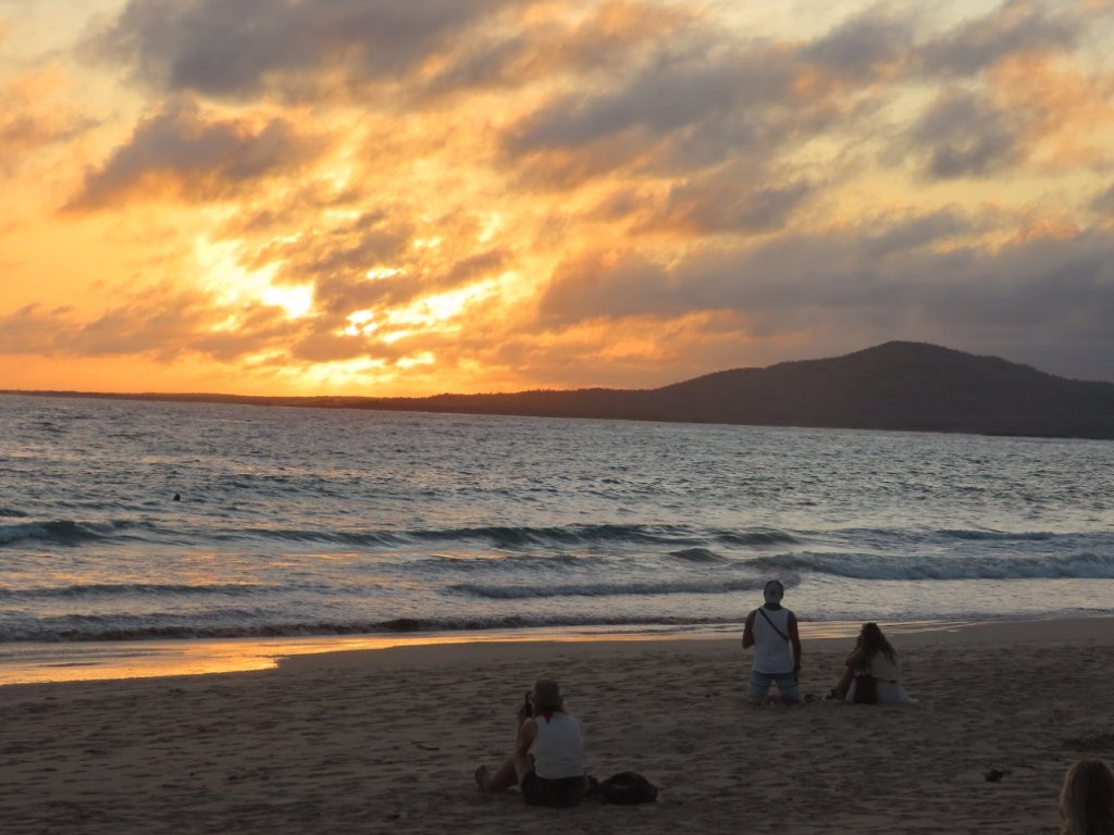 Golden sunset light spreads across the ocean as people sit on the sand watching waves roll toward shore. Slow evenings like this are part of what makes Isabela feel so different from the busier Galapagos islands.