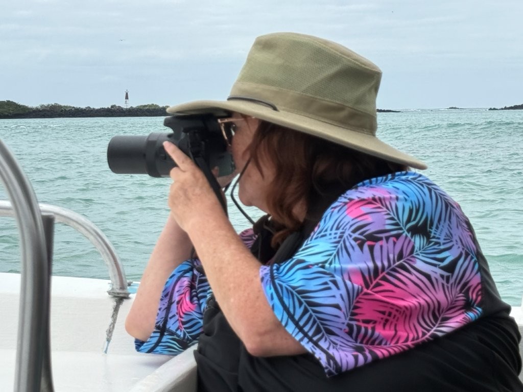 Kari takes a photo with her camera while riding on a boat in the ocean. She's wearing her swim shirt and wide-brimmed hat for sun protection. Knowing what to pack for the Galapagos means a few smart choices.