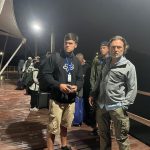 Passengers wearing ferry lanyards wait on a dark, wet pier before sunrise with luggage lined up behind them. Early morning departures are common when taking the Galapagos ferry, and the check-in process feels easier when you know what to expect.