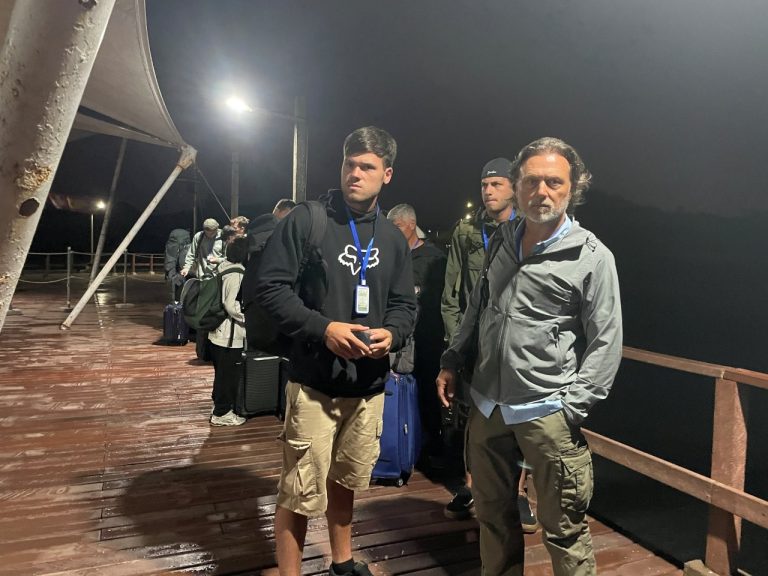 Passengers wearing ferry lanyards wait on a dark, wet pier before sunrise with luggage lined up behind them. Early morning departures are common when taking the Galapagos ferry, and the check-in process feels easier when you know what to expect.
