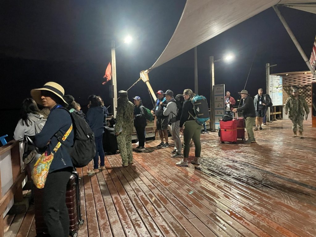 A line of passengers with backpacks and rolling bags waits under bright pier lights before boarding the early ferry from Isabela. Arriving early gives you more time to check in, clear biosecurity, and settle into the rhythm of Galapagos ferry travel.