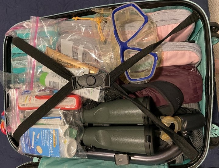 A suitcase is packed with a snorkel mask, binoculars, sunscreen, pink packing cubes and other colorful items. Knowing what to pack for the Galapagos is a key part of a successful trip.
