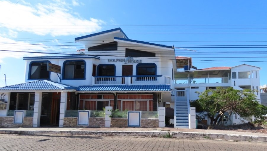 A white-and-blue hotel building with balconies and large windows stands along a quiet paved street on San Cristobal Island. Dolphin House stood out as one of the strongest value hotels for travelers in San Cristobal.