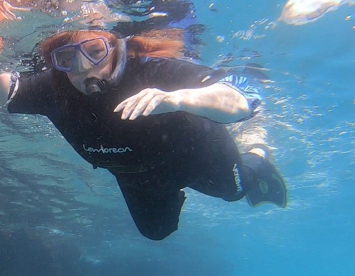 Kari in a black wetsuit snorkeling in the clear water of Gardner Bay.