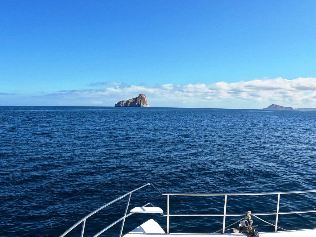 A boat approach Kicker Rock in the distance of the blue Pacific Ocean.