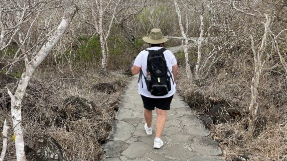 Kari walks away down a stone Galapagos trail wearing a sun hat, backpack, shorts, and comfortable walking shoes. This photo shows why simple hiking clothes, sun protection, and a daypack belong on a Galapagos packing list.