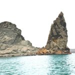 Wide scenic view of Pinnacle Rock and Bartolome Island’s volcanic coastline reflected in calm turquoise water.