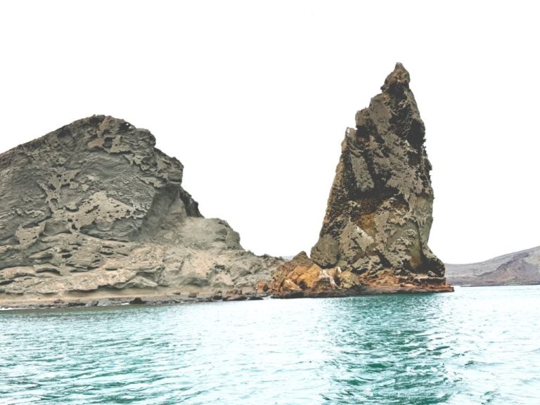 Wide scenic view of Pinnacle Rock and Bartolome Island’s volcanic coastline reflected in calm turquoise water.