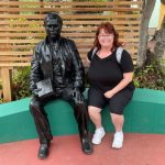 A smiling woman sits beside a bronze statue of Charles Darwin on a curved bench outside the visitor center. Taking photos around the Charles Darwin Visitor Center added a fun personal memory to our low-cost time on Santa Cruz Island.