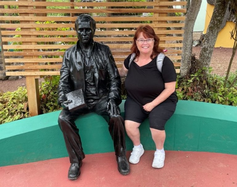 A smiling woman sits beside a bronze statue of Charles Darwin on a curved bench outside the visitor center. Taking photos around the Charles Darwin Visitor Center added a fun personal memory to our low-cost time on Santa Cruz Island.