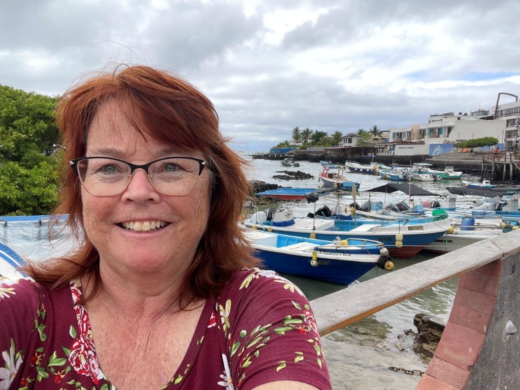 Kari takes a selfie beside colorful fishing boats and waterfront buildings along the Puerto Ayora harbor. Walking the waterfront ended up being one of our favorite free things to do on Santa Cruz Island because there was always something interesting happening nearby.