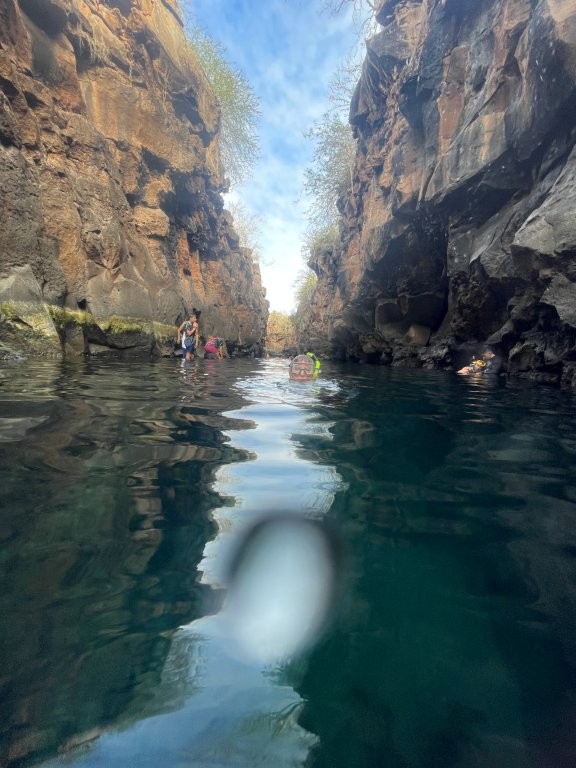 Swimmers float through a narrow volcanic canyon filled with deep blue-green water between towering lava rock walls at Las Grietas. Snorkeling at Las Grietas was one of the most memorable low-cost adventures we experienced on Santa Cruz Island.