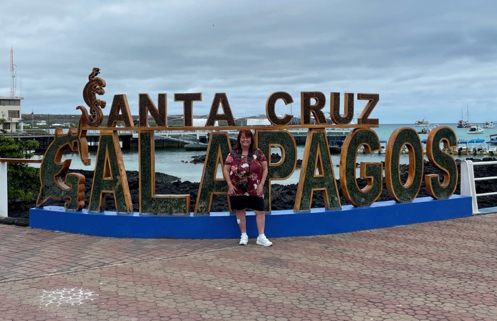 Kari stands smiling in front of the large Santa Cruz Galapagos sign overlooking the waterfront in Puerto Ayora. Visiting the waterfront became one of my favorite free things to do in Santa Cruz Galapagos during our time on the island.