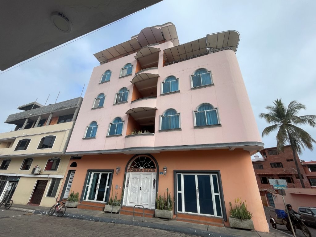 A tall pastel-colored hotel with balconies rises above a quiet Puerto Ayora street lined with small buildings and palm trees. Torre Mar Galapagos Boutique Suites is a flexible option for where to stay in Santa Cruz Galapagos because it offers everything from rooms to apartments and larger suites.