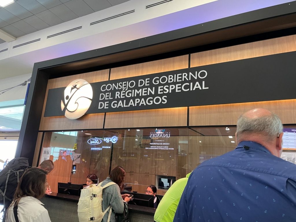 Travelers stand at the Galapagos Government Council counter inside the Quito airport for TCT verification. This is where passengers confirm or complete the Transit Control Card before flying to the Galapagos.