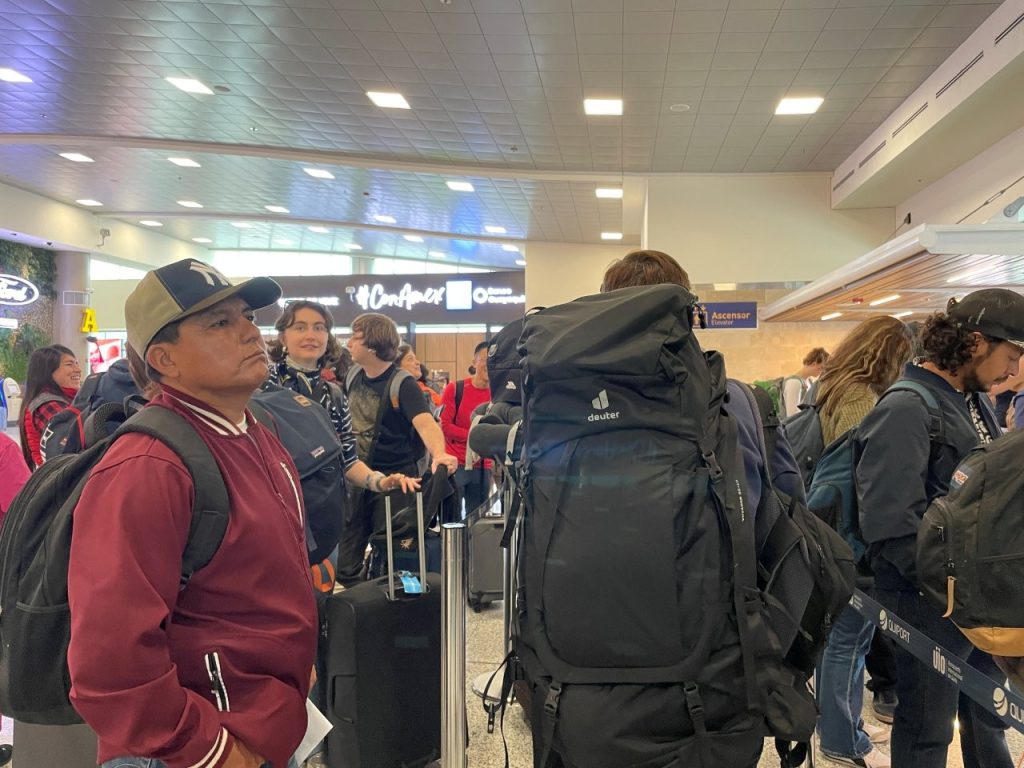 Travelers with backpacks and rolling luggage wait in a crowded airport line for Galapagos TCT processing. This line shows why the Galapagos airport process can take longer than a typical domestic flight.