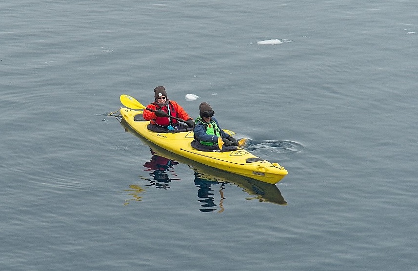 Two people sit in a bright yellow kayak with chunks of ice floating nearby in the cold waters of Antarctica