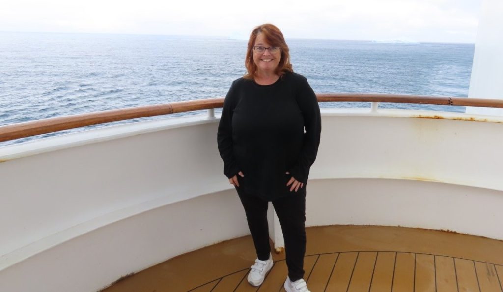 Kari stands on the ship wearing a black shirt, black pants, and athletic shoes before adding insulating layers. Starting with lightweight clothing made it easy to build warmth without packing bulky winter gear.