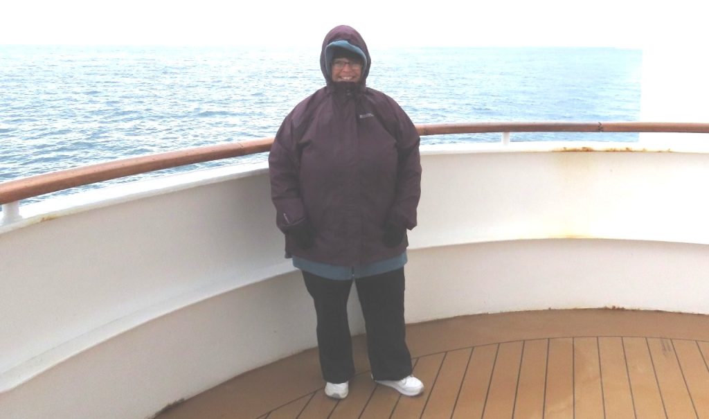 Kari wears a waterproof rain jacket with the hood up while standing outside on deck. The rain jacket was only needed once in Ushuaia but was still worth packing for Antarctica's unpredictable weather.