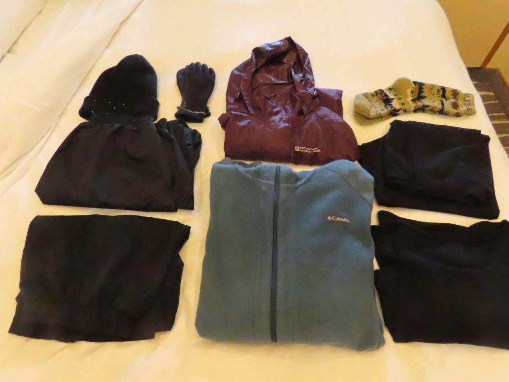 Cold-weather clothing, gloves, socks, rain gear, fleece, and leggings are neatly arranged on a bed. Seeing everything together makes it easier to judge how little clothing was actually needed for a scenic cruise.