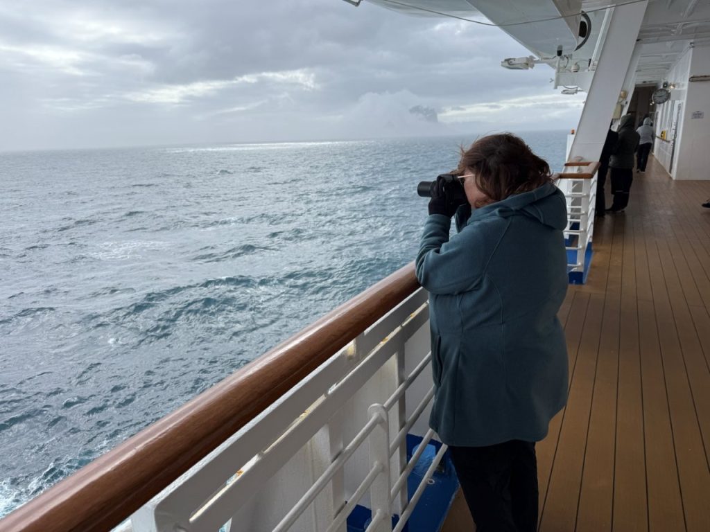 Kari photographs the Antarctic coastline from the promenade deck with a camera and zoom lens. Spending hours with a camera in hand made packing lightweight gloves and warm layers even more important.